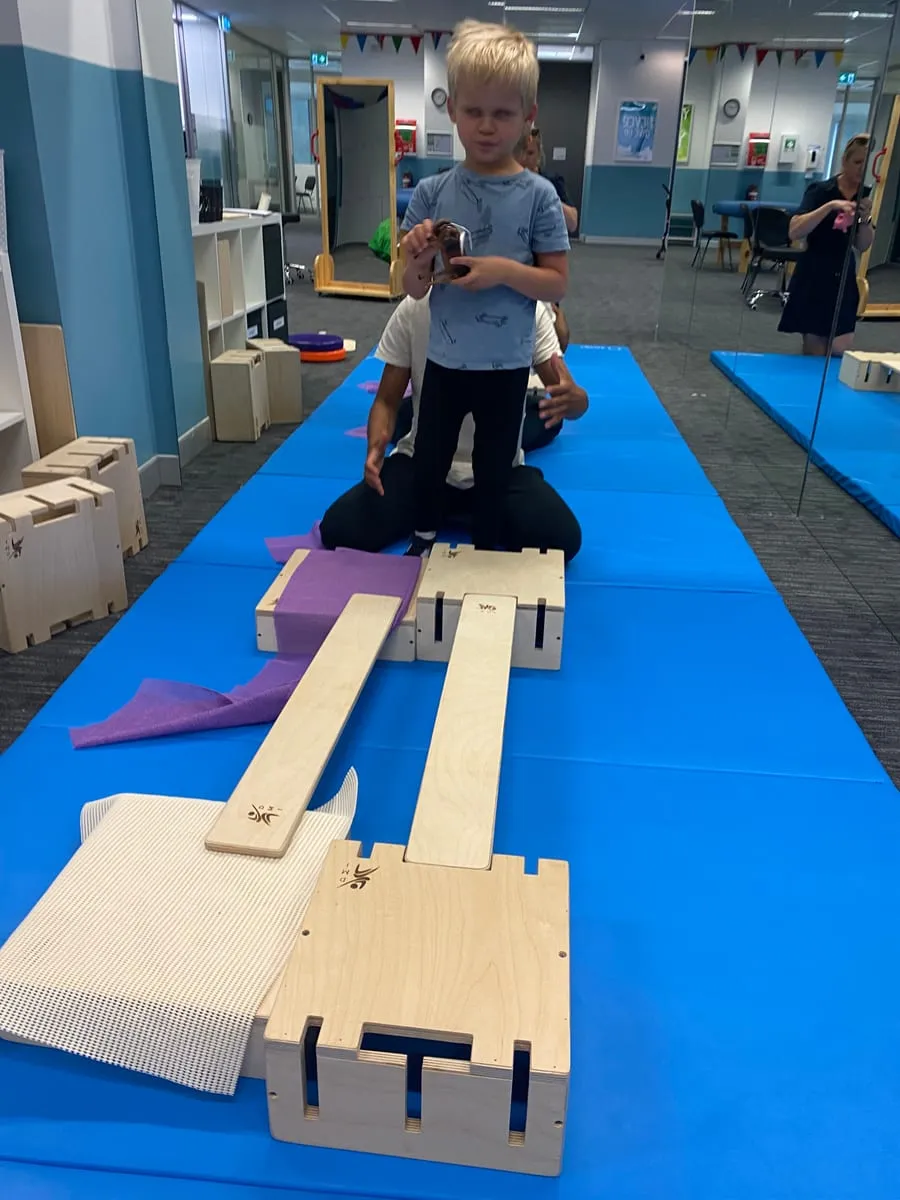 A smiling boy walking along a balance beam during a therapy session.