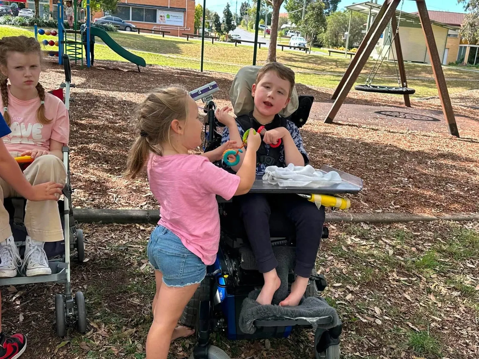 Children with STXBP1 disorders, some in wheelchairs, playing with their siblings and friends at a park.