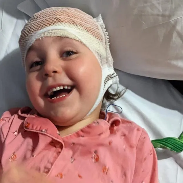 Coco smiling broadly in a hospital bed, her head wrapped in EEG wires.