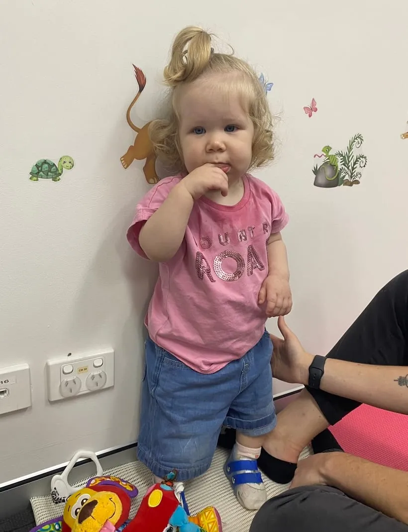 A little girl standing on her own against a wall during therapy.